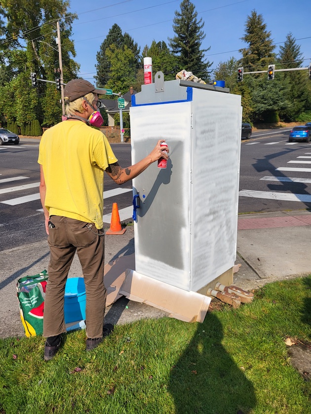 Madison spraying the base coat of white paint on an electrical box.