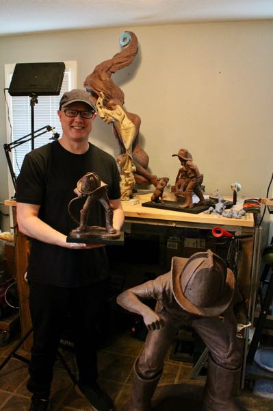 Jeremy holding statue of boy drinking from firehose with firehouse helmet on.