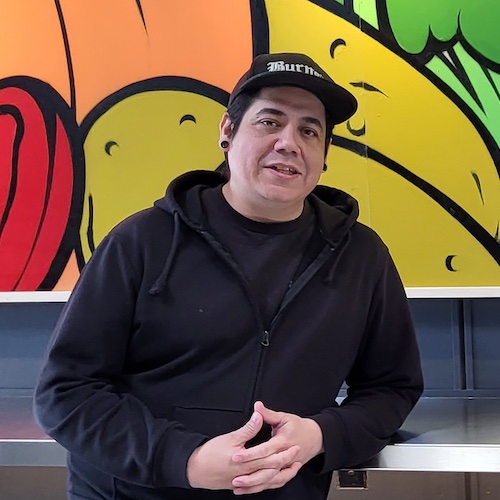 Ricardo Alvarez in front of hiw mural of fruits and vegetables.