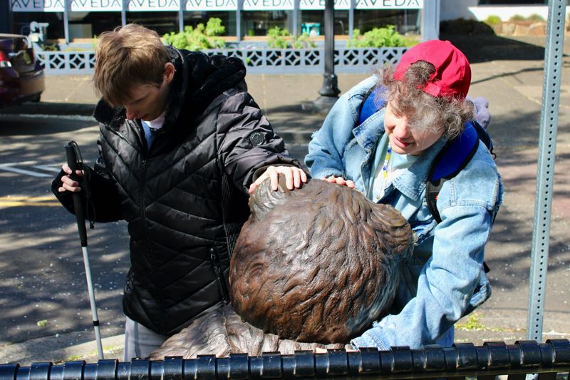 Two people touching Teddy the bear statue.