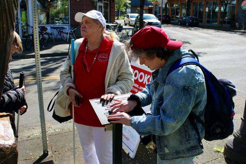 Two people reading braille sign next to Blue.